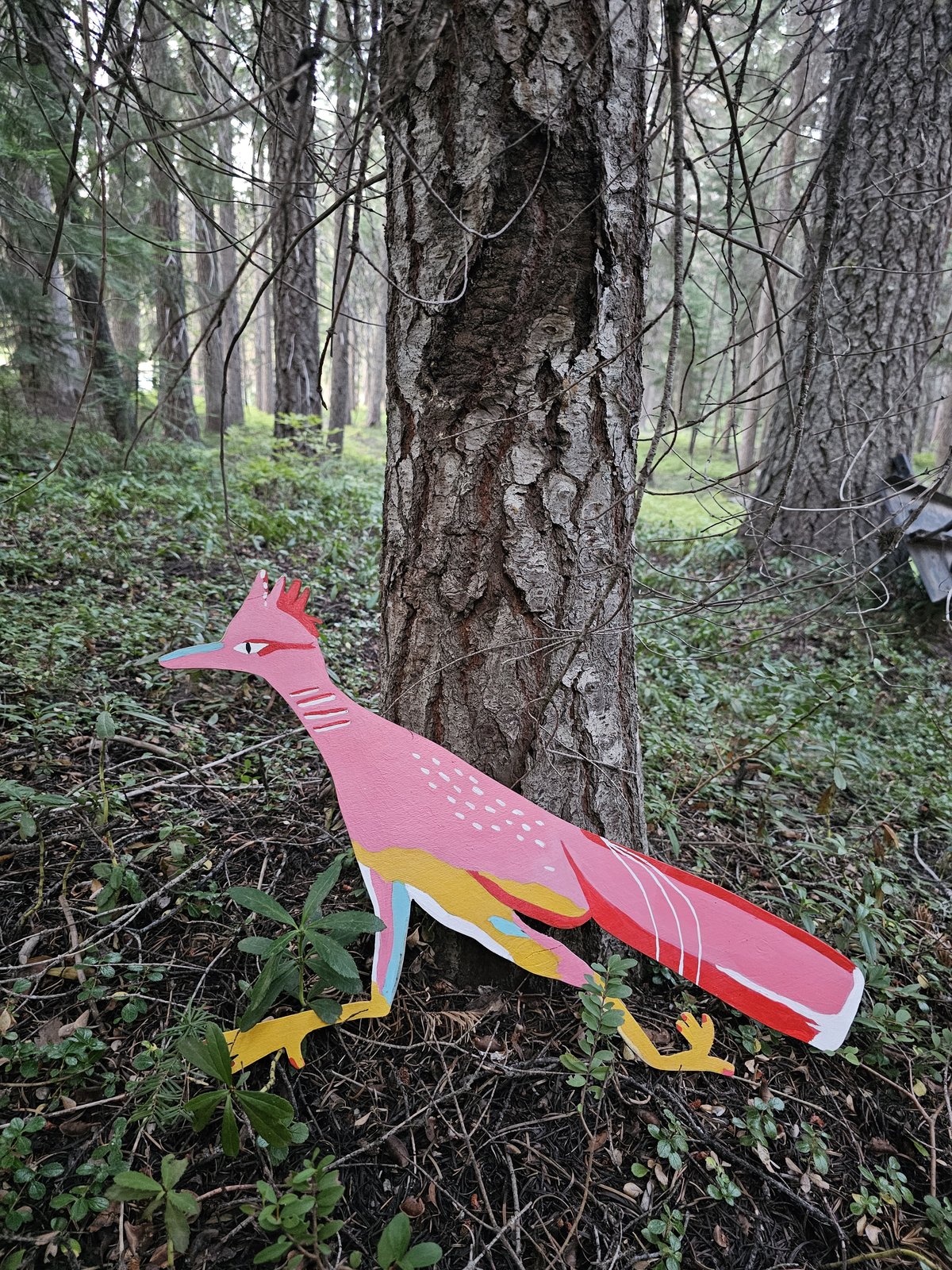 Hand-painted wood panel roadrunner resting against a tree trunk in the forest