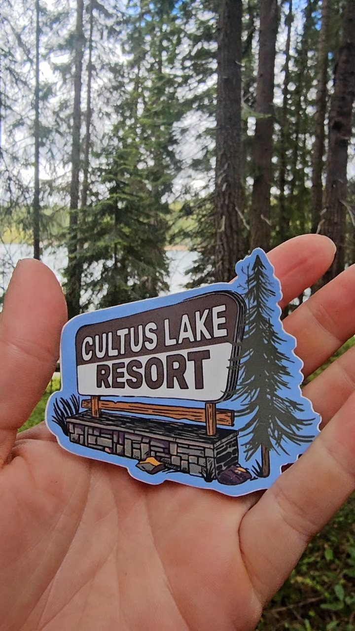 Illustrated Cultus Lake Resort sign sticker held up in a forest