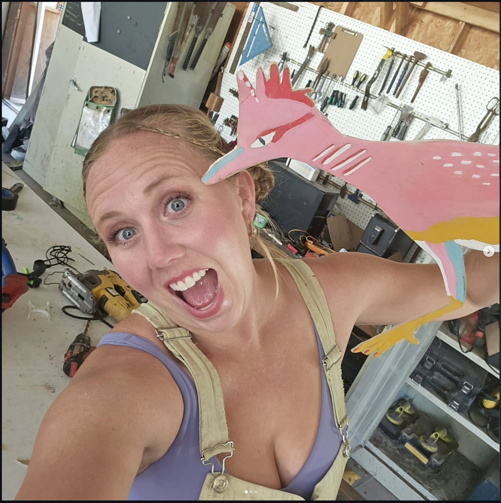 Artist holding up the finished hand-painted roadrunner wood panel in her workshop